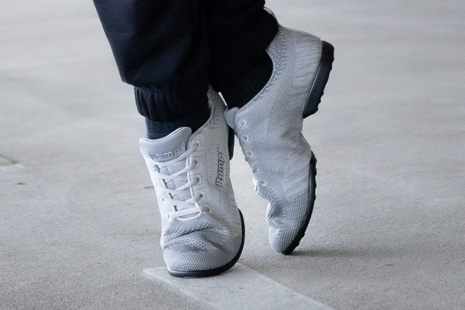 Person in grauen Turnschuhen und schwarzen Hosen läuft auf einer hellen Oberfläche.